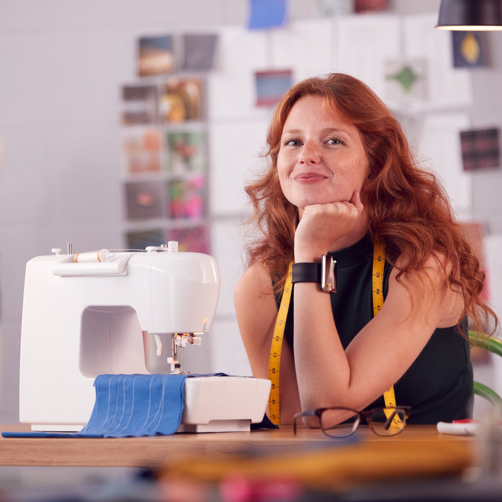 Mujer sonriente en un taller de costura, apoyada sobre su mano junto a una máquina de coser profesional con tela azul.